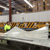 Two men in high visibility shirts in the Metroll wareouse with a large sheet of metal getting ready to cut out some custom flashings for a customer.